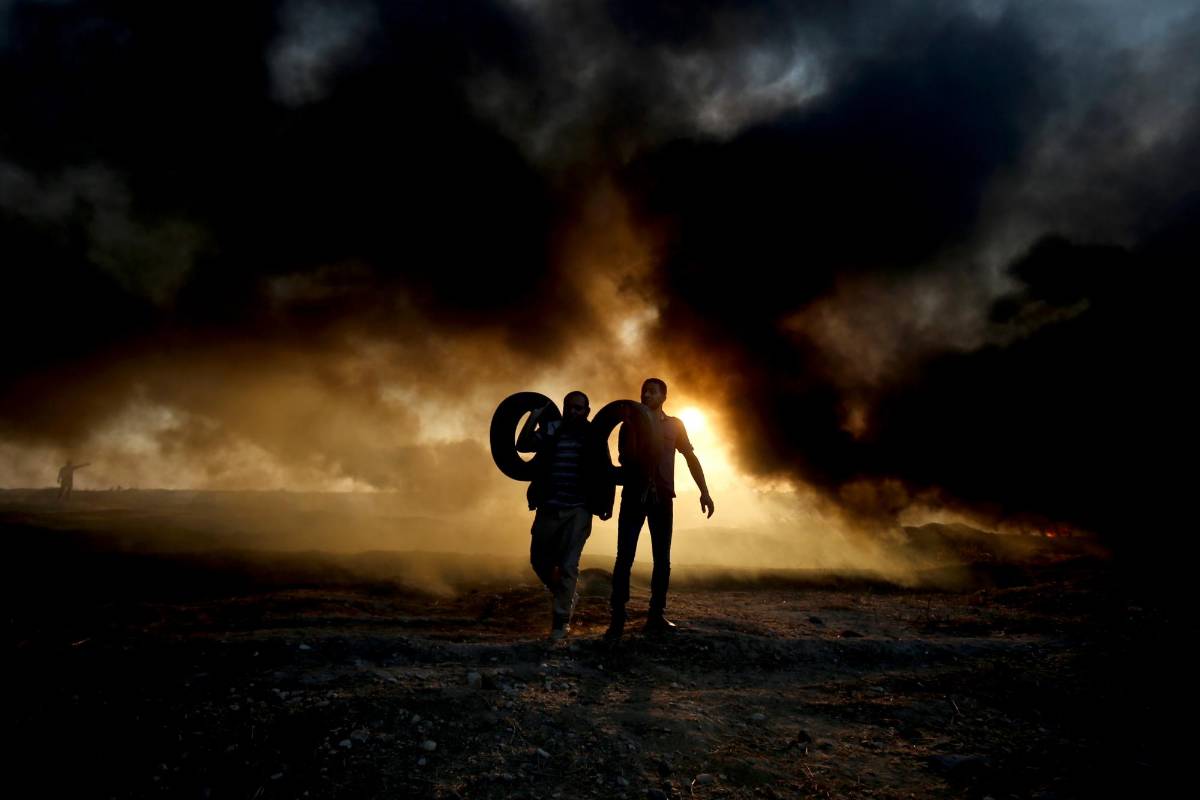 Manifestantes palestinos sostienen unas llantas mientras el humo emana de los neumáticos quemados en la frontera de Gaza con Israel FOTO AFP