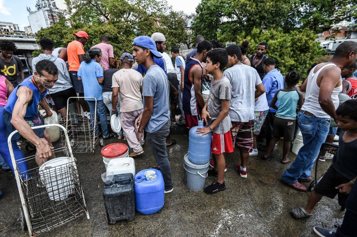 Las personas con latas y cubos esperan a recolectar agua de un canal de aguas residuales en el río Guaire en Caracas, mientras un apagón masivo continúa afectando algunas áreas del país. Foto: Juan Barreto