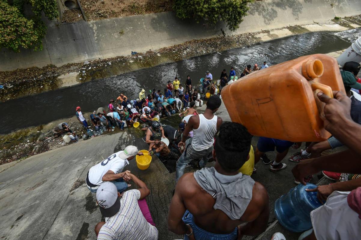 La gente recolecta agua de un canal de aguas residuales en el río Guaire en Caracas, mientras un apagón masivo continúa afectando algunas áreas del país. Foto: Juan Barreto