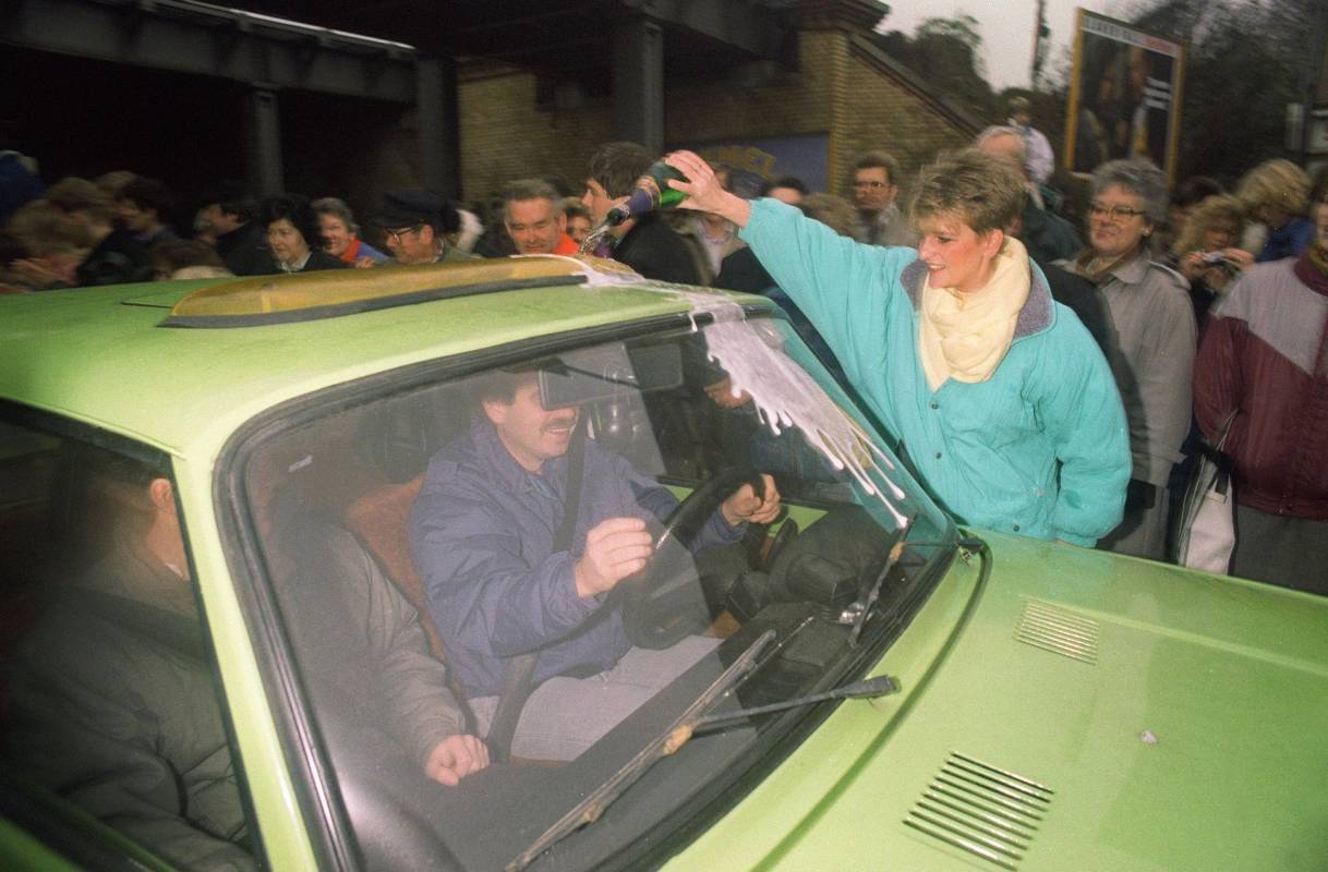 Una berlinesa occidental (der.) da la bienvenida a un berlinés oriental mientras vierte champán en su automóvil en Wollangstrasse, donde se abrió un punto de cruce hacia el oeste. Foto de archivo tomada el 13 de noviembre de 1989. FOTO AFP