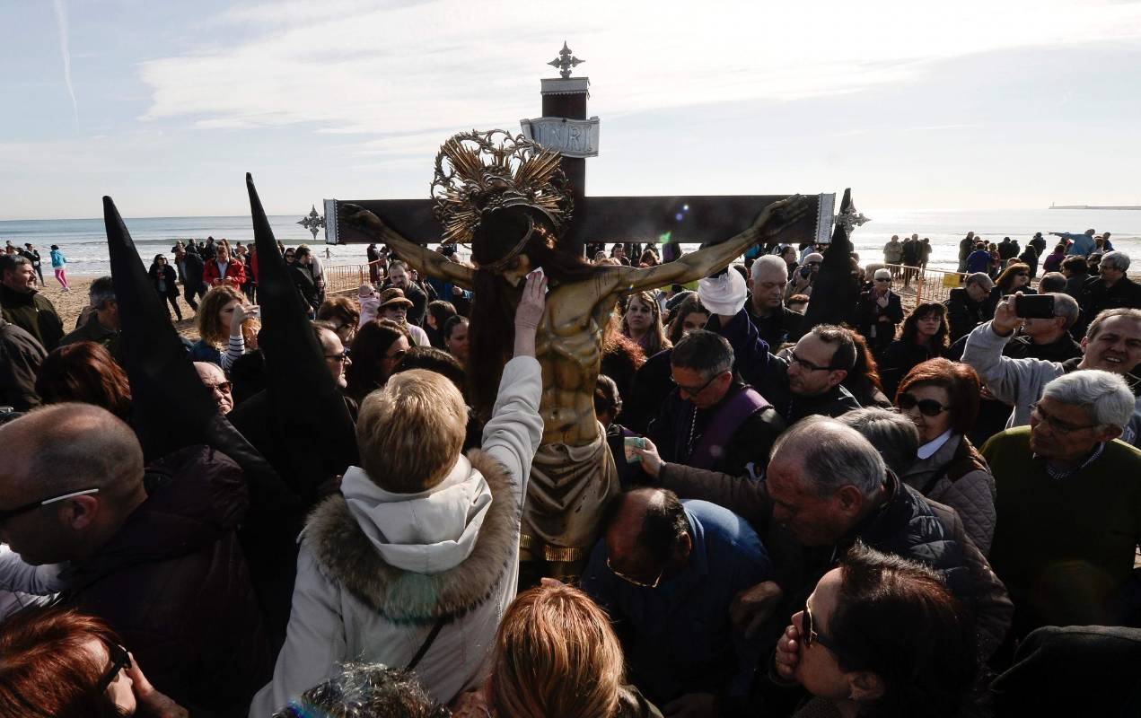 Varios fieles de la iglesia católica se aproximan a tocar el crucifijo expuesto en una playa en Valencia (España) durante los días de Semana Santa. FOTO AFP