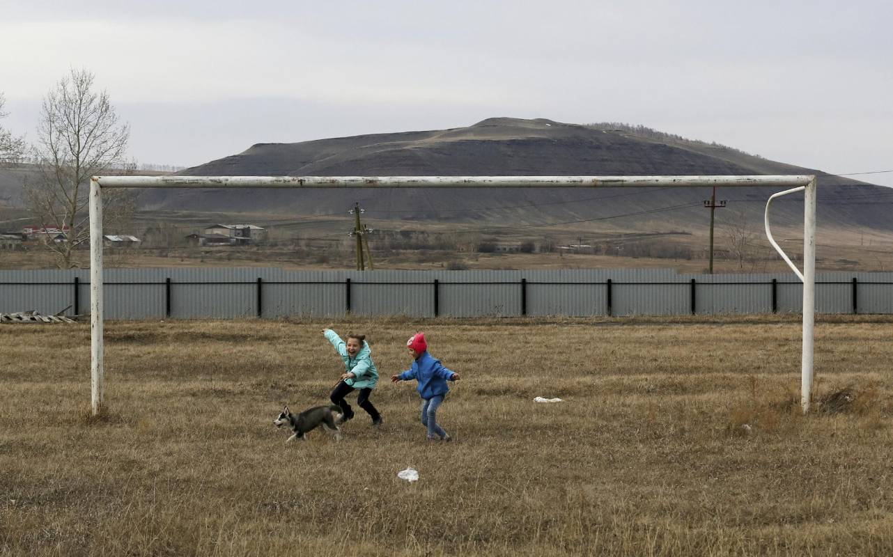 Unos niños juegan con un cachorro cerca de un arco en un campo de fútbol en el asentamiento siberiano de Novosyolovo, región de Krasnoyarsk, Rusia. Foto: REUTERS / Ilya Naymushin 