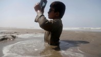 Un niño con discapacidad está sentado a medio enterrar en la orilla del río Indo, y utiliza una placa de rayos X para observar un eclipse solar parcial, siguiendo el consejo de un médico de permanecer en la arena durante el suceso. FOTO EFE
