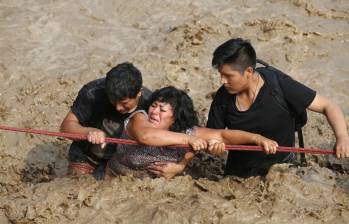 Una mujer es asistida para poder cruzar una calle en la región de Huachipa, donde se desbordó el río Huayco. FOTO reuters