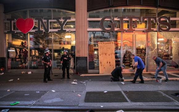 Los oficiales de policía de la ciudad de Nueva York hacen guardia mientras los trabajadores cubren una ventana rota en una tienda. FOTO AFP
