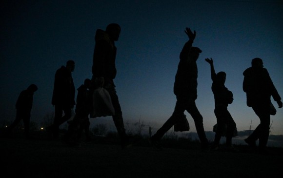 Refugiados y migrantes saludan mientras caminan hacia un campamento en el lado turco de la frontera entre Turquía y Grecia cerca de la puerta de cruce de Pazarkule en la provincia de Edirne el 7 de marzo de 2020. FOTO: AFP