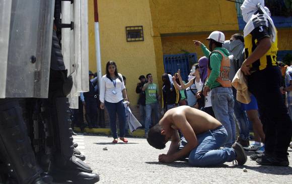 Un joven con sangre en su pecho se arrodilla frente a la policía después de que un estudiante de 14 años de edad, Kluiver Roa, muriera de un disparo en la cabeza durante una protesta en San Cristóbal. FOTO REUTERS