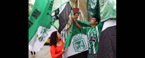 Las Mellizas del rebusque verdolaga | Manuel Saldarriaga | Aracelly Zapata le da rienda suelta al rebusque, con la ventaja de objetos que recuerden al Nacional. Los clientes le piden hasta pequeñas camisetas para el perro. Aquí la acompaña un cliente, Giovanni Mazo, y su ahijado Sebastián. Ella estaba ayer vestida de rojo, "para llamar la atención". Está en Buenos Aires.