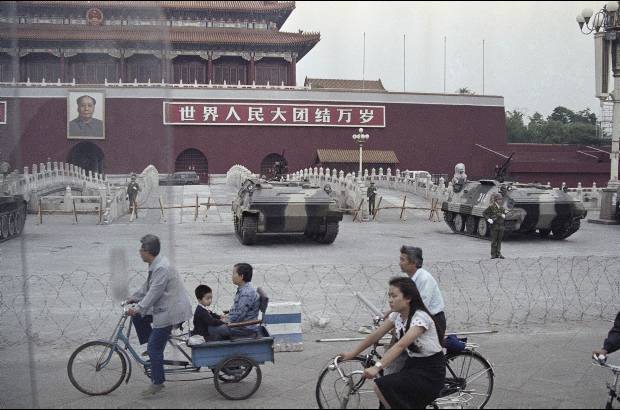 AP - 13 de junio de 1989. Gente en bicicleta pasan frente a varios veh&#237;culos blindados estacionados en frente de la puerta de Tiananmen.