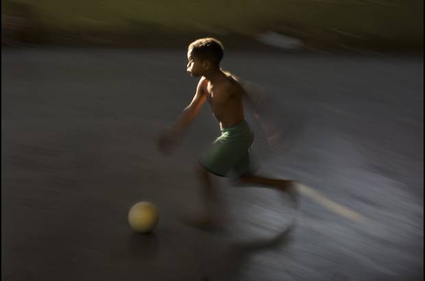 AP - Un joven corre tras un balón de fútbol en una calle del barrio la Mangueira, un sector pobre de Río de Janeiro, Brasil.