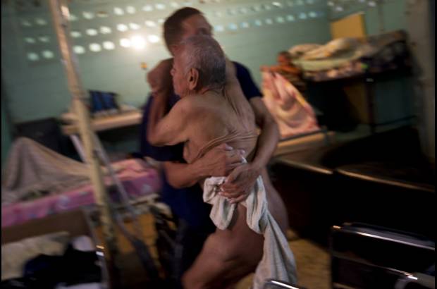 Reuters - Danny Martínez, un paciente en rehabilitación de drogas, ayuda a pasar a un anciano de su silla de ruedas a la cama, después de bañarlo en el centro de rehabilitación para adictos a las drogas y el alcohol Nosotros Unidos en Caracas. Este centro está financiado por una iglesia cristiana, y ha sido un modelo para las instituciones del Estado con la mismo objetivo.