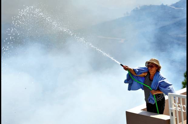 AP - Una mujer lanza agua alrededor de su casa durante un incendio forestal en el sur de Rodas, Grecia. Las autoridades declararon el estado de emergencia despu&#233;s de un incendio destruy&#243; unas 4.000 hect&#225;reas de bosques y tierras de cultivo.