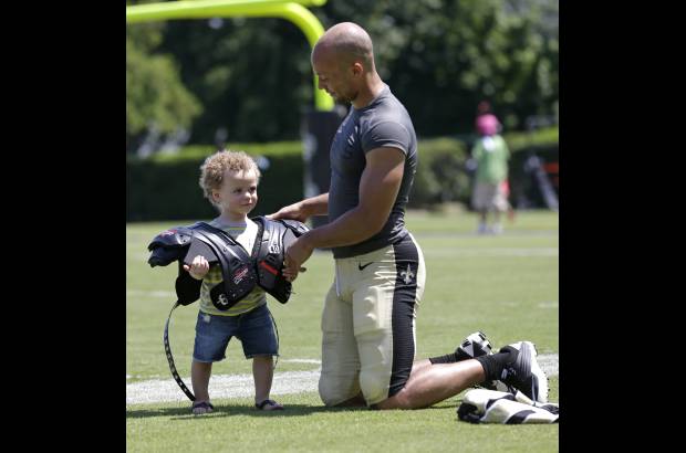 AP - El defensa de los Santos de New Orleans Chris Carr pone sus hombreras a su hijo, de 21 meses de edad, Octavian Carr, en pleno campo de entrenamiento de la NFL en Metairie, Louisiana.