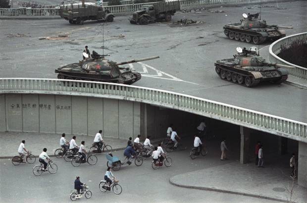 AP - 6 de junio 1989. Ciclistas pasan frente a grafitis que dec&#237;an &quot;movilizar a todos los ciudadanos para aplastar la ley marcial, proteger Beijing&quot;, debajo de un puente donde veh&#237;culos blindados tomaban posici&#243;n en Changan Blvd.