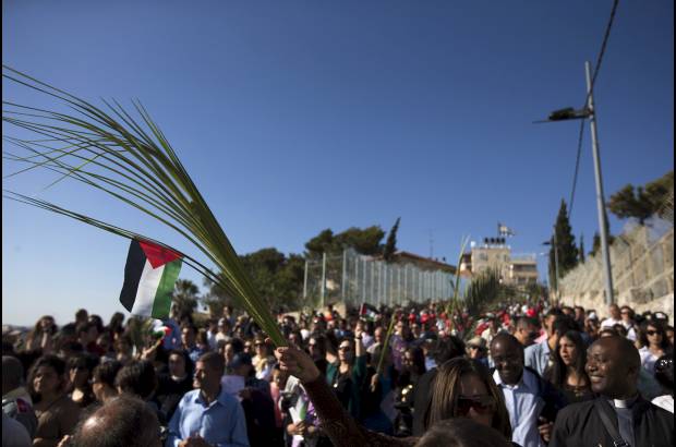 Reuters - Una cat&#243;lica tiene una hoja de palma con una bandera palestina durante la procesi&#243;n de Domingo de Ramos en el Monte de los Olivos en Jerusal&#233;n.