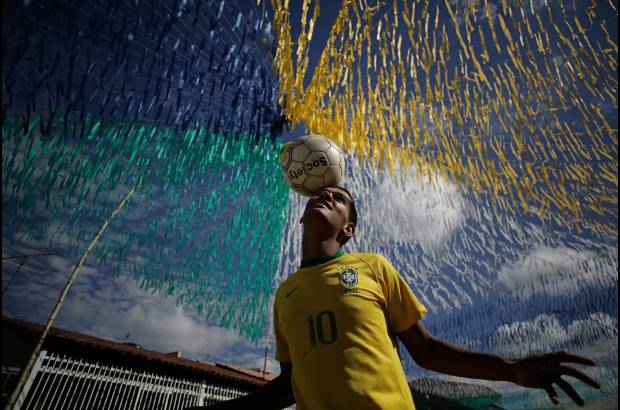 AP - Joao Paulo, de 16 años, se divierte con un balón en una calle adornada para la próxima Copa del Mundo, en el suburbio Ceilandia de Brasilia, Brasil.