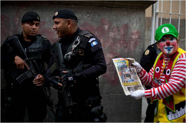 AP - Un oficial de polic&#237;a sonr&#237;e mientras un payaso sostiene un peri&#243;dico que representa una escena del crimen y dice en tono de broma: &quot;La polic&#237;a, siempre en las noticias&quot;.