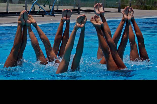 Henry Agudelo - Mientras dentro del agua de la piscina de nado sincronizado del Complejo Acuático, doce niñas, entre los 20 y los 28 años, practican de 7 de la mañana a la 1 de la tarde, afuera, tres entrenadoras (una canadiense, una bioelorusa y otra china), dos fisiólogos, un médico, una fisioterapeuta, un entrenador de acrobacias y una mánager, trabajan con sus computadores, filamadoras y toda clase de ayudas audiovisuales.