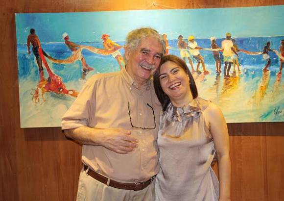 Cortesía - La artista Clara Inés Pérez en su exposición Manifiesto de luz y color en el Hotel Portón, en compañía del también pintor Carlos Sánchez. En el fondo la obra Pescadores.