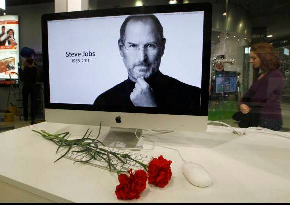 Reuters - Claveles rojos frente a una pantalla que muestra un foto de Steve Jobs, fue tan solo uno de los miles de tributos que recibió el cofundador de Apple, una de las muertes más sentidas de 2011.