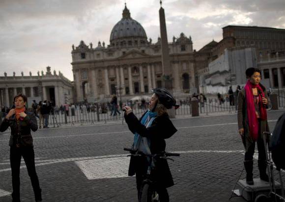 AP - Un ciclista toma una foto de periodistas de la televisi&#243;n internacional informando desde las afueras de la plaza de San Pedro, en el Vaticano.