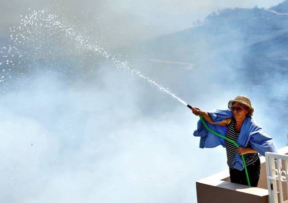 AP - Una mujer lanza agua alrededor de su casa durante un incendio forestal en el sur de Rodas, Grecia. Las autoridades declararon el estado de emergencia despu&#233;s de un incendio destruy&#243; unas 4.000 hect&#225;reas de bosques y tierras de cultivo.
