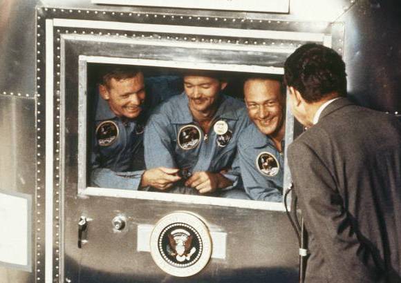 AP - NASA - 24 de julio de 1969. El presidente Richard Nixon, a la derecha, saluda a los astronautas del Apolo 11 en la furgoneta de cuarentena, a bordo del USS Hornet, después del amerizaje y recuperación.
