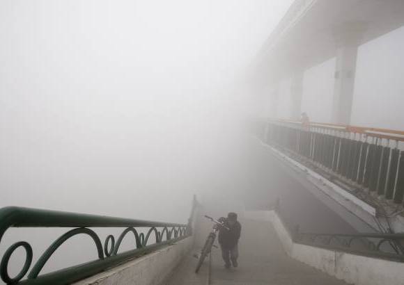 AP - Un hombre empuja una bicicleta para subir a un puente en un día de extrema polución en Harbin, noreste de China.