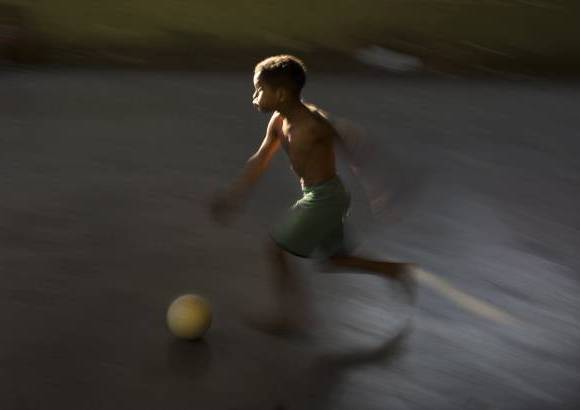 AP - Un joven corre tras un balón de fútbol en una calle del barrio la Mangueira, un sector pobre de Río de Janeiro, Brasil.