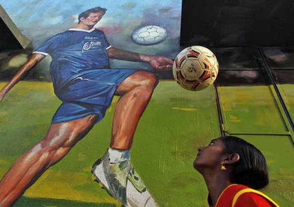 AP - En India, una niña cabecea un balón frente a un mural del excapitán de la selección de ese país, Baichung Bhutia, en un parque infantil en Chennai, India.