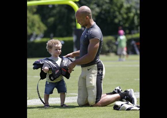 AP - El defensa de los Santos de New Orleans Chris Carr pone sus hombreras a su hijo, de 21 meses de edad, Octavian Carr, en pleno campo de entrenamiento de la NFL en Metairie, Louisiana.