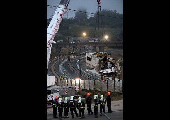 Reuters - Los bomberos ven como una grúa retira un vagón de las pistas en el lugar del accidente cerca de Santiago de Compostela, el noroeste de España.
