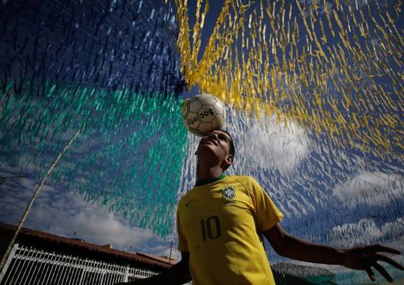 AP - Joao Paulo, de 16 años, se divierte con un balón en una calle adornada para la próxima Copa del Mundo, en el suburbio Ceilandia de Brasilia, Brasil.