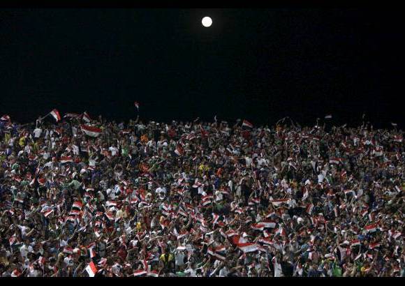 AP - Esta imagen es en Bagdad, Irak. La Luna asoma por encima de los aficionados al fútbol que animan a su equipo durante un partido amistoso en el estadio Al-Shaab en Bagdad, donde Irak ganó 2-1 sobre Siria.