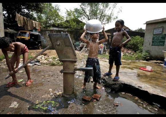 AP - Muchachos de Bhubaneswar, India, se bañan con agua de una bomba de mano.