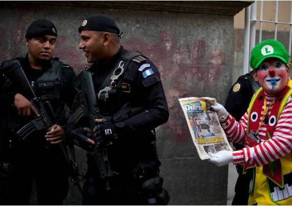 AP - Un oficial de polic&#237;a sonr&#237;e mientras un payaso sostiene un peri&#243;dico que representa una escena del crimen y dice en tono de broma: &quot;La polic&#237;a, siempre en las noticias&quot;.