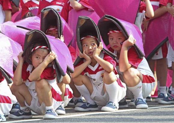 AP - Ni&#241;os taiwaneses cubren su cabeza para evitar el sol durante un ensayo para las celebraciones del D&#237;a Nacional en frente de la Oficina Presidencial en Taipei, Taiw&#225;n.