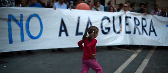 Una niña corre junto a una pancarta durante una protesta contra la intervención extranjera en Siria, en Pamplona, al norte de España. FOTO AP