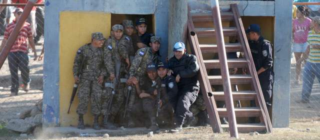 Los presos en A.L. purgan penas en trampas mortales | Efectivos de la Policía y miembros de la prensa se refugian de los palos y piedras lanzados por familiares de los reos afectados por el incendio en la cárcel de Comayagua. FOTO AP