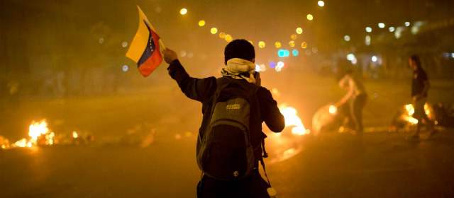 Un manifestante contra el gobierno de Maduro sostiene una bandera de Venezuela frente a una barricada ardiendo en el barrio Altamira de Caracas. Este sábado se esperan manifestaciones de protesta en todo el país. FOTO REUTERS
