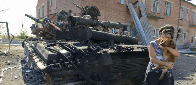 Una mujer sostiene un perro al lado de un tanque destruido en el patio de un jardín de infantes en la localidad de Talakovka, Mariupol, un día después de que Kiev y prorrusos rebeldes firmaron el alto el fuego. FOTO AFP