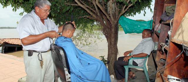 La gente de Caucasia y su lucha contra el invierno | Pablo Emiro trabaja a la sombra de un árbol. Al fondo, el río Cauca, que en diciembre se desbordó y derribó su local. FOTO JAIME PÉREZ.