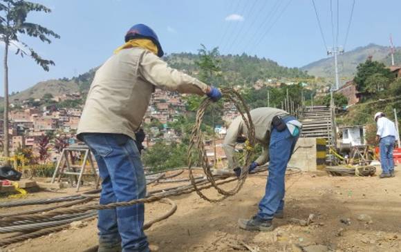 Dos trabajadores del Metro sostienen parte del cable que fue instalado en la comuna ocho de Medellín. CORTESÍA Metro de Medellín.