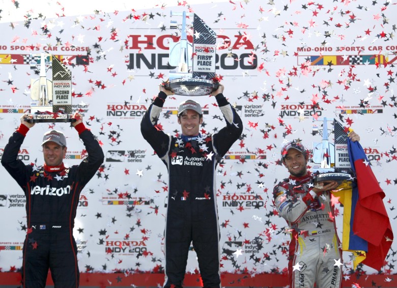 Carlos Muñoz se mostró orgulloso con su bandera colombiana en el podio del circuito en Mid Ohio, al lado de dos campeones como Will Power (segundo) y Simón Pagenaud (vencedor). FOTO AP 