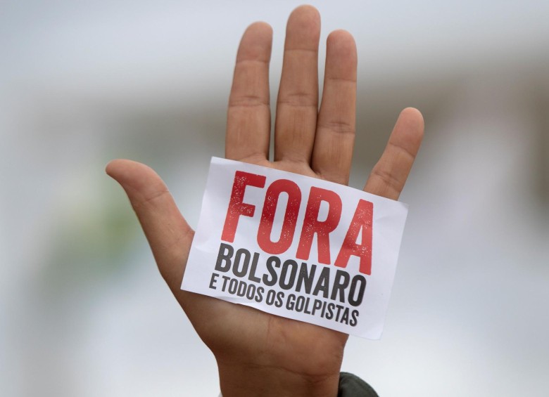 Una mano que muestra un pequeño cartel en el que se lee “Fuera Bolsonaro y todos los golpistas”, durante una protesta contra el presidente de Brasil, Jair Bolsonaro, el pasado miércoles 20 de mayo, en el Palacio de Planalto en Brasilia. FOTO: EFE