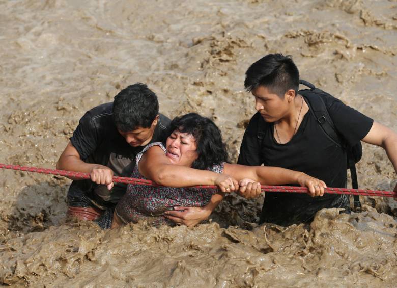 Una mujer es asistida para poder cruzar una calle en la región de Huachipa, donde se desbordó el río Huayco. FOTO reuters