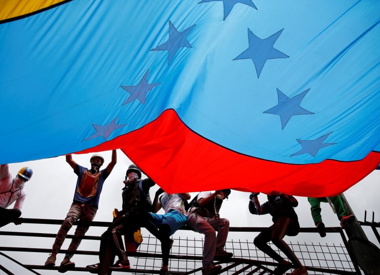 Algunos manifestantes subieron a las rejas de la Base Aérea Francisco de Miranda, para sostener una gran bandera Venezolana. FOTO: REUTERS