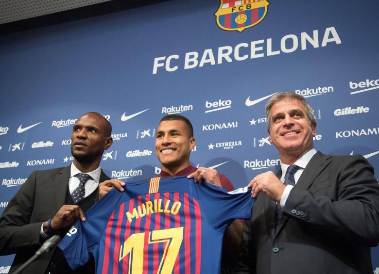 Éric Abidal, secretario técnico de Barça y Jordi Mestre, vicepresidente del club, posan con Murillo. FOTO EFE