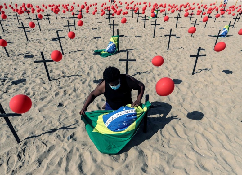 n activista instala una bandera de Brasil en una representación escénica de la ONG Río de Paz por las víctimas del COVID-19 hoy, en la playa de Copacabana en Río de Janeiro (Brasil). Con mil globos rojos en las arenas de la playa y cien de ellos fijados en cien cruces negras se rindió homenaje a los 100 mil brasileños fallecidos por la pandemia de coronavirus y se manifestaron en contra de la forma en que el Gobierno ha gestionado la crisis sanitaria. FOTO: EFE