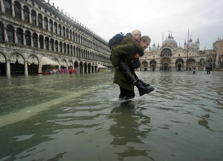 Un hombre carga a una mujer durante la inundación en la Plaza de San Marco en Venecia. FOTO EFE